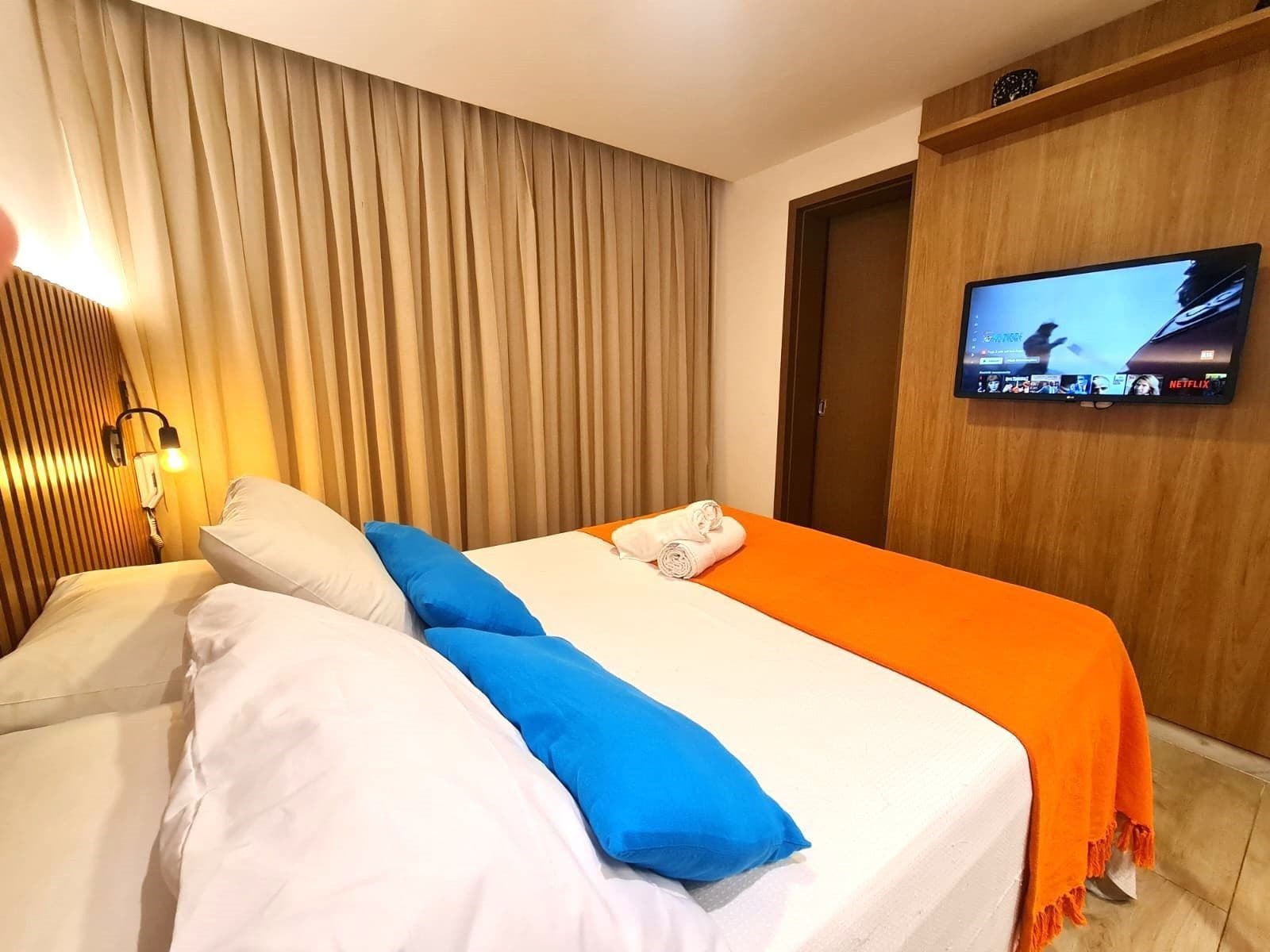 Une chambre d’hôtel avec un lit, un téléviseur fixé au mur et un rideau.