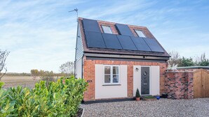 Une petite maison en briques, dotée de panneaux solaires sur le toit, d’une allée en gravier et d’un jardin bien entretenu.