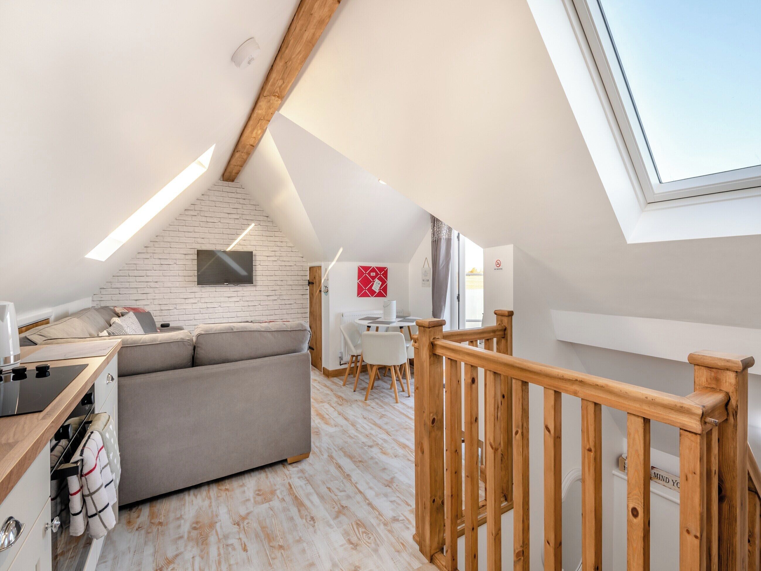 Un dormitorio tipo loft moderno con techo inclinado, televisor empotrado, escalera de madera y un tragaluz grande.