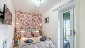 Une chambre à coucher avec une tête de lit capitonnée, une grande fenêtre offrant une belle vue et une porte donnant sur l’extérieur.