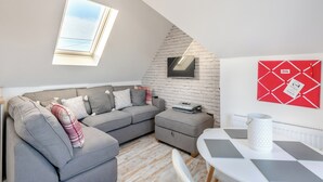 Une chambre de style loft moderne, avec un canapé gris, une petite table, un téléviseur fixé sur un mur en briques et une lucarne.