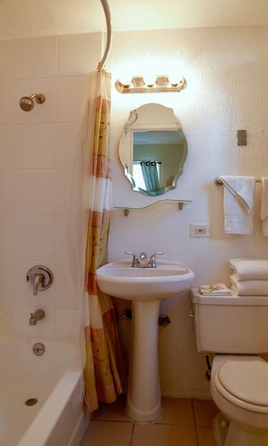 A bathroom with a bathtub, a pedestal sink, a toilet, a mirror, and a shower curtain. - Baltic Hotel (Miami Beach)
