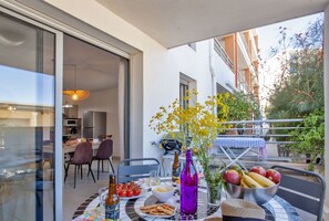 A balcony with a dining table set for two, featuring a bowl of fruit, a bottle, and a vase with yellow flowers. - Appartement "Fiora" en centre-ville de Calvi - 2 4 personnes (Calvi)