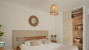 A bedroom with a wooden bed, a bedside table, a hanging light fixture, a mirror, and built-in wooden shelving. - Appartement "Fiora" en centre-ville de Calvi - 2 4 personnes (Calvi)