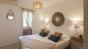 A bedroom with a bed, bedside lamps, a mirror, and a window with curtains. - Appartement neuf "Magnolia", terrasse pergola, jardin privatif - 2 4 pers (Calvi)