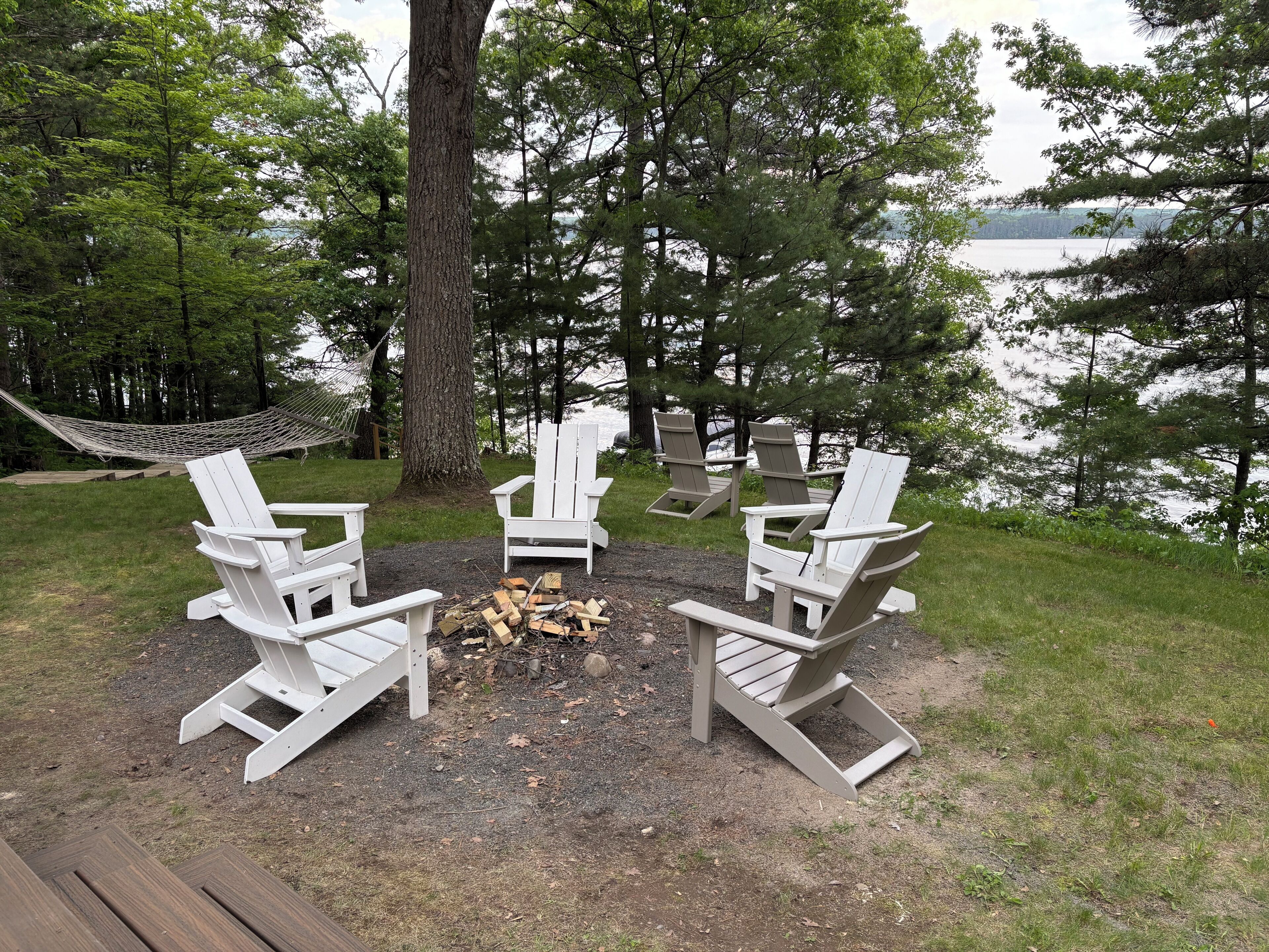 En sittplats vid sjön med Adirondack-stolar och en eldstad.