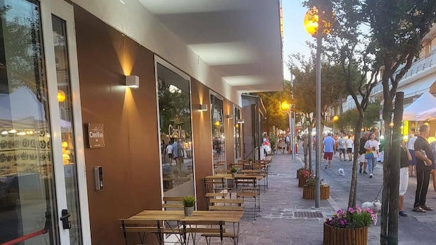An outdoor café with wooden tables and chairs, a stone-paved walkway, and flower planters. - HOTEL CRISVAN (Rimini)