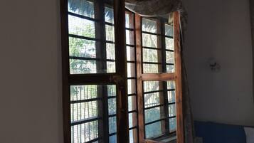 Une pièce avec un lit, une petite fenêtre à cadre en bois et un rideau.