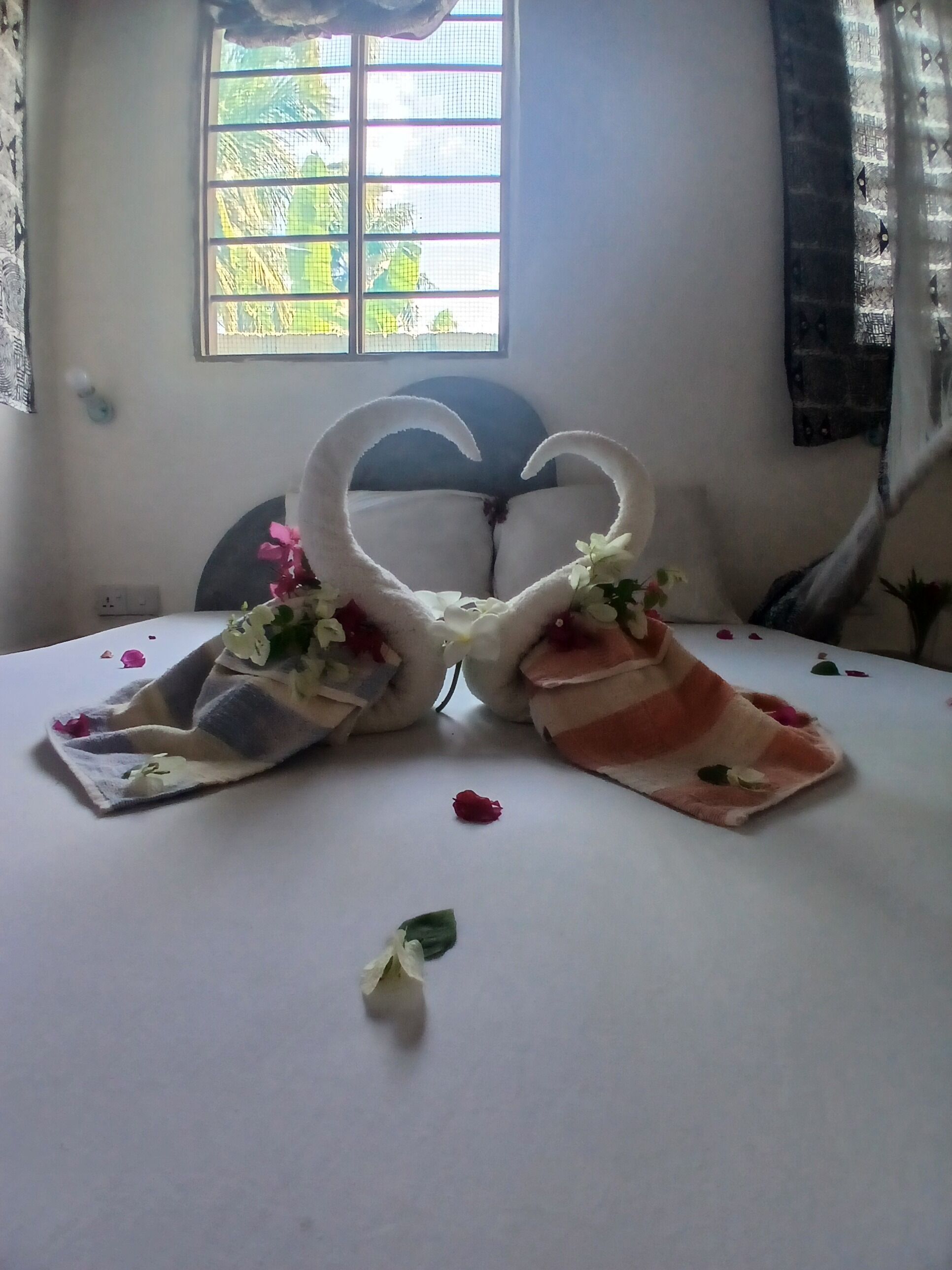 A bed with a heart-shaped towel arrangement, a window with a view, and a bedside table with a vase.