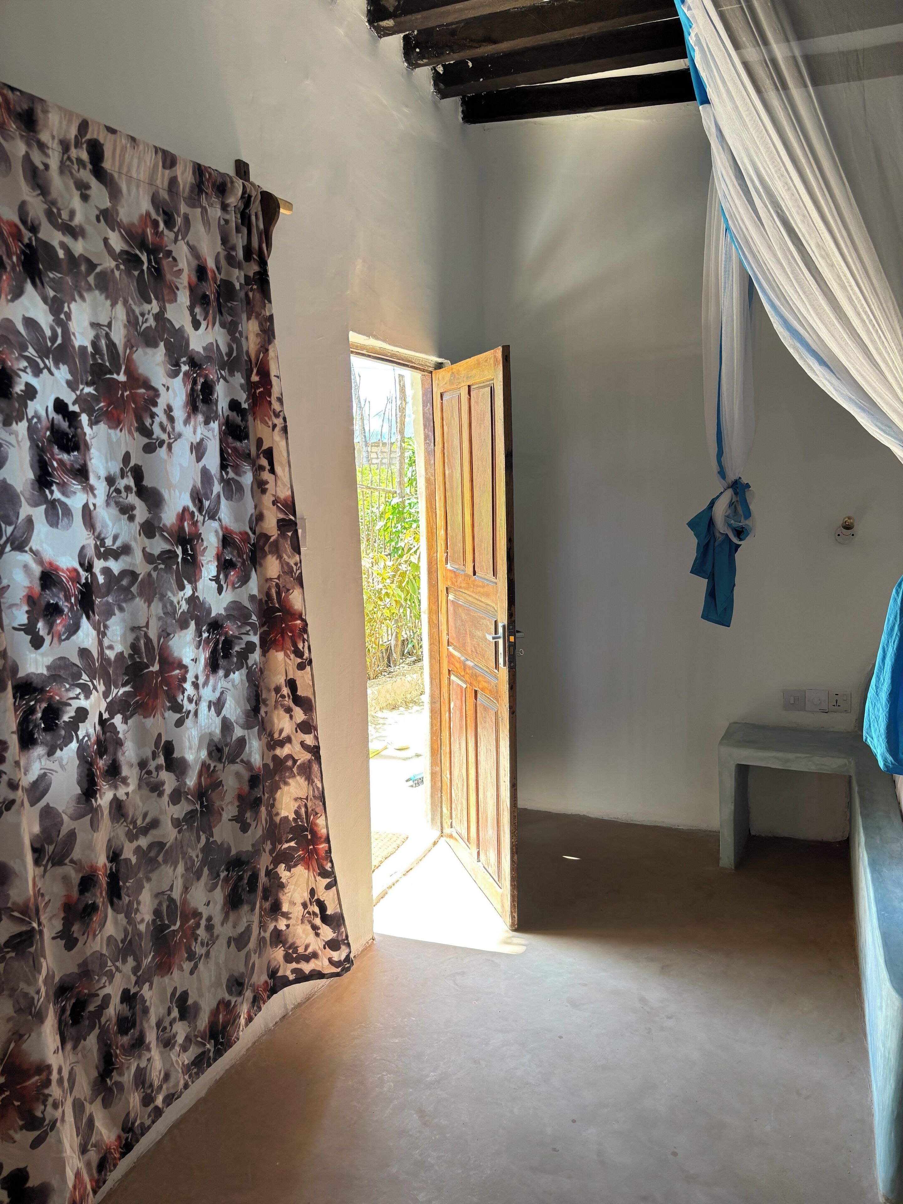 A room with a wooden door, a small white stool, and a curtain with a floral pattern.