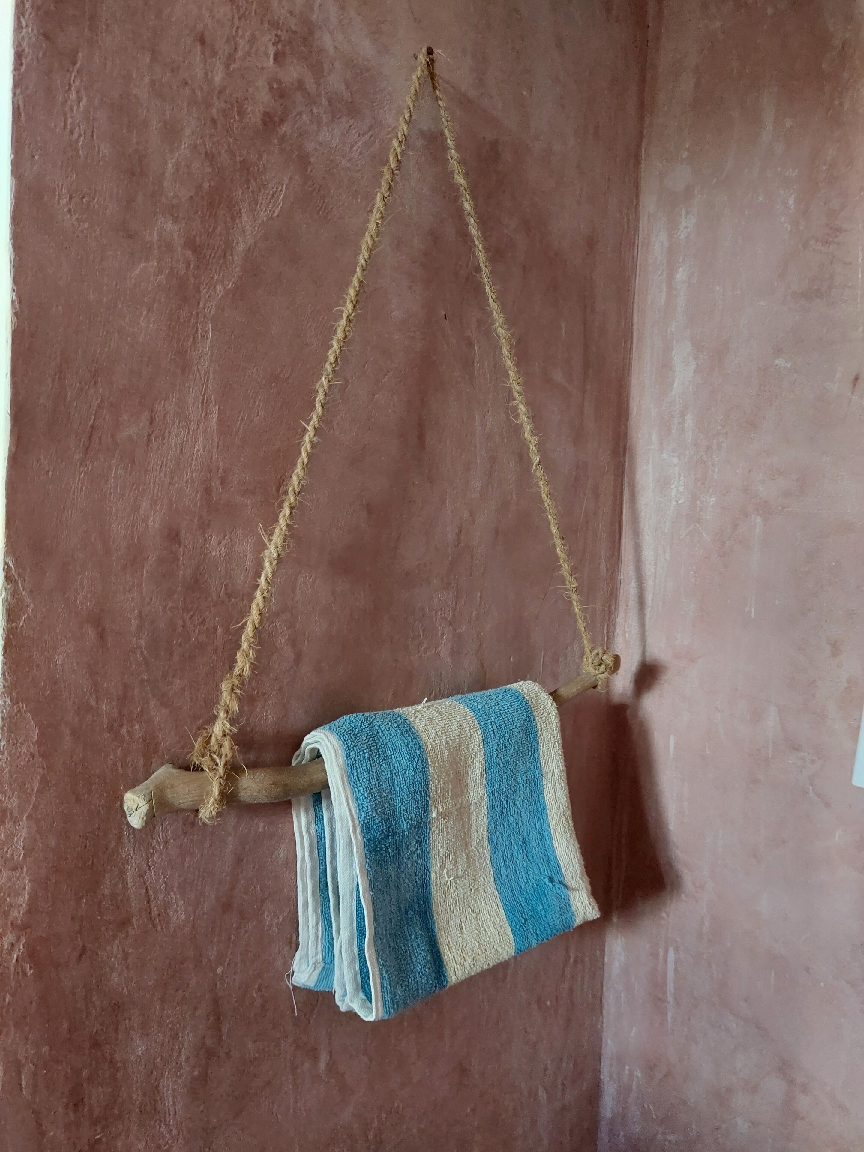 Una toalla colgada de una rama de madera frente a un muro con textura.