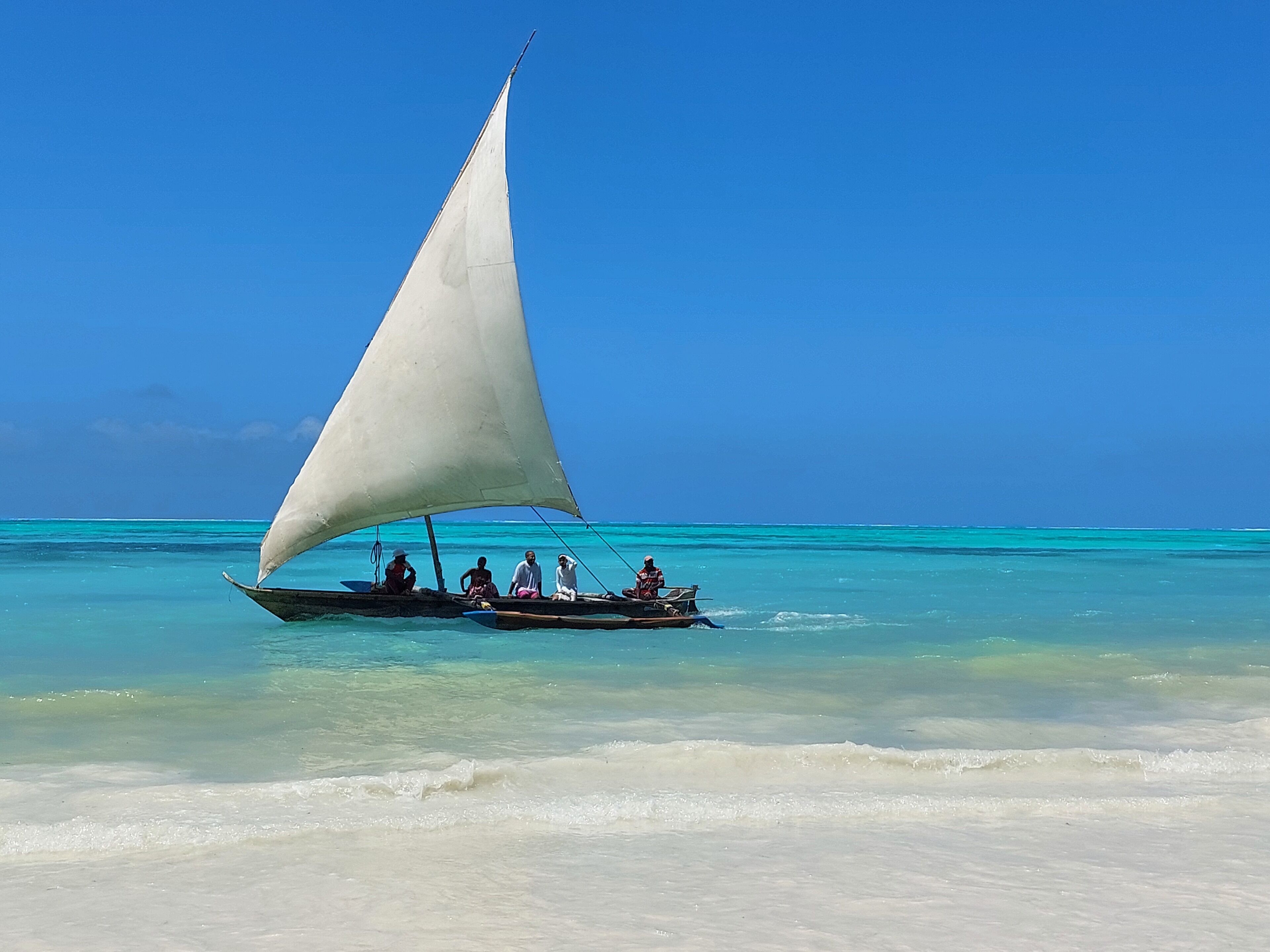 A boat with a large sail on a clear turquoise sea.