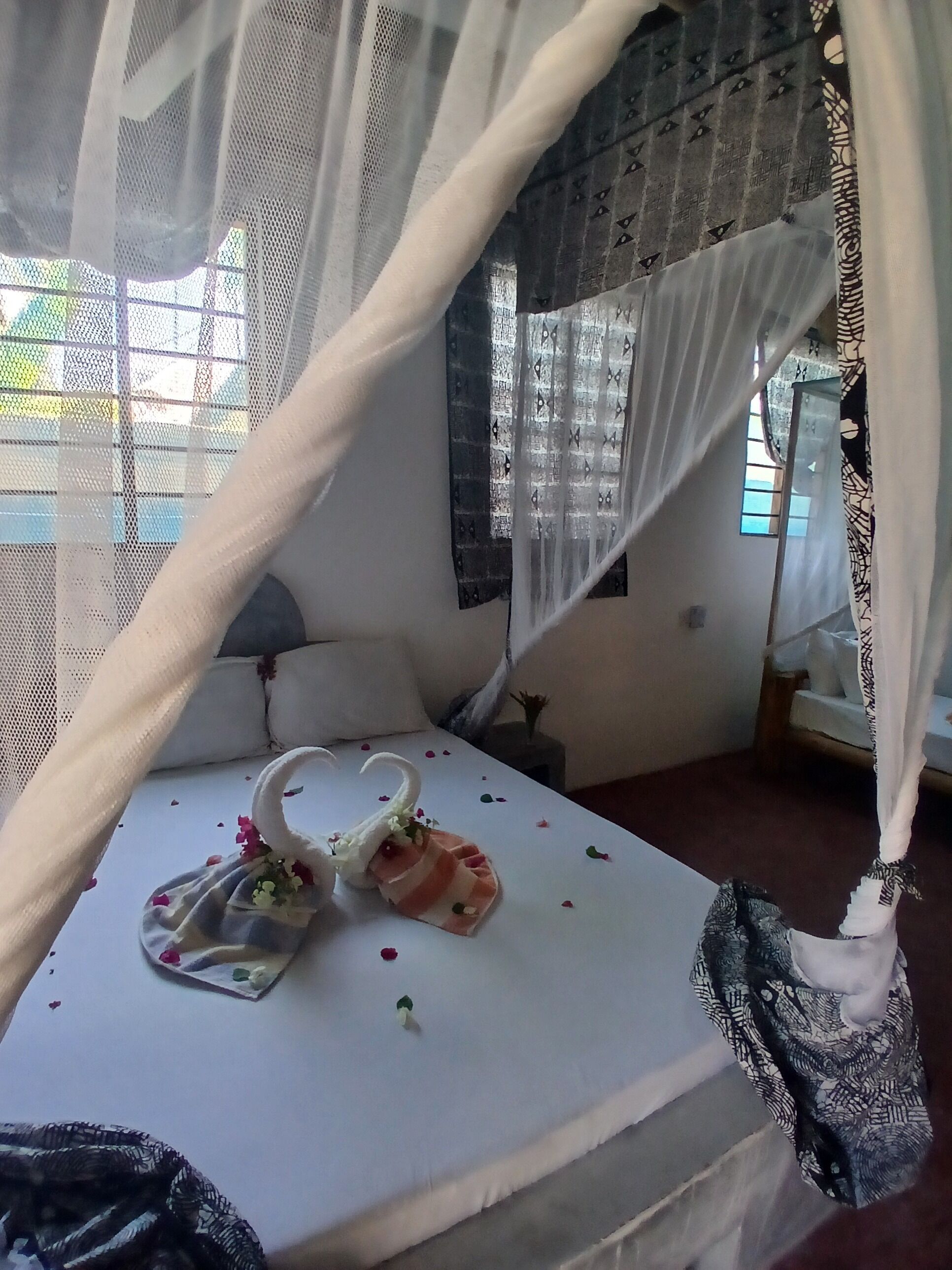 A bed with a canopy, pillows, a bedside table, and a window with patterned curtains.