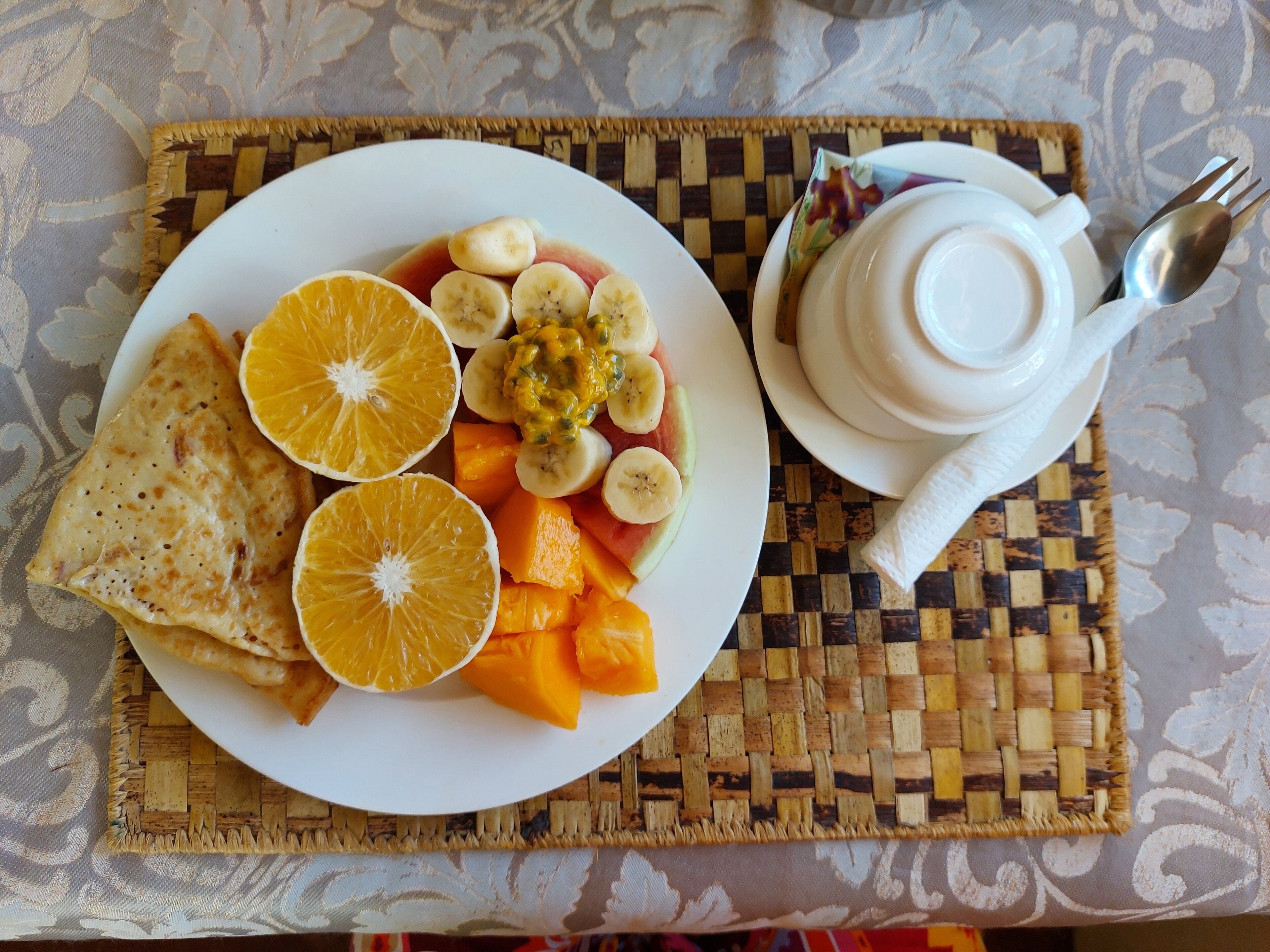 A plate with fruit and a folded item, possibly a crepe, on a woven placemat.