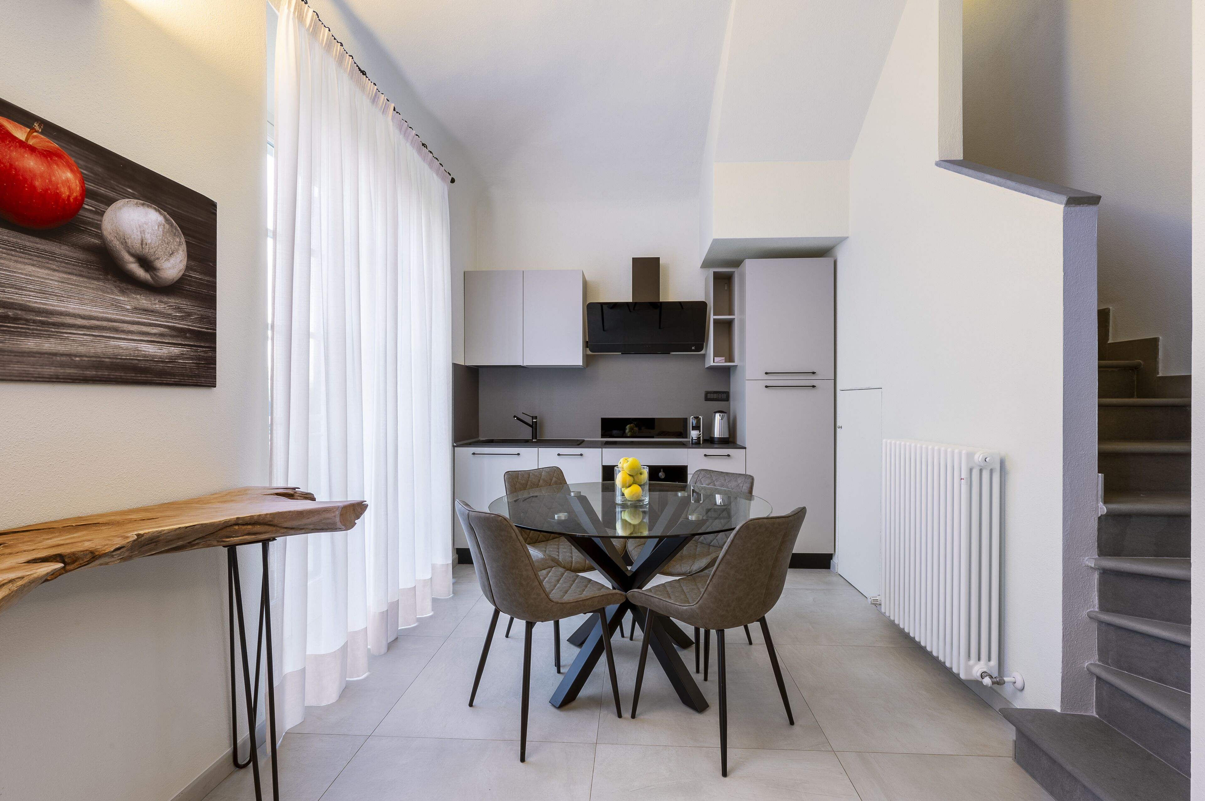 A modern kitchen with white cabinets, a central island, and a dining area with a glass table and chairs.