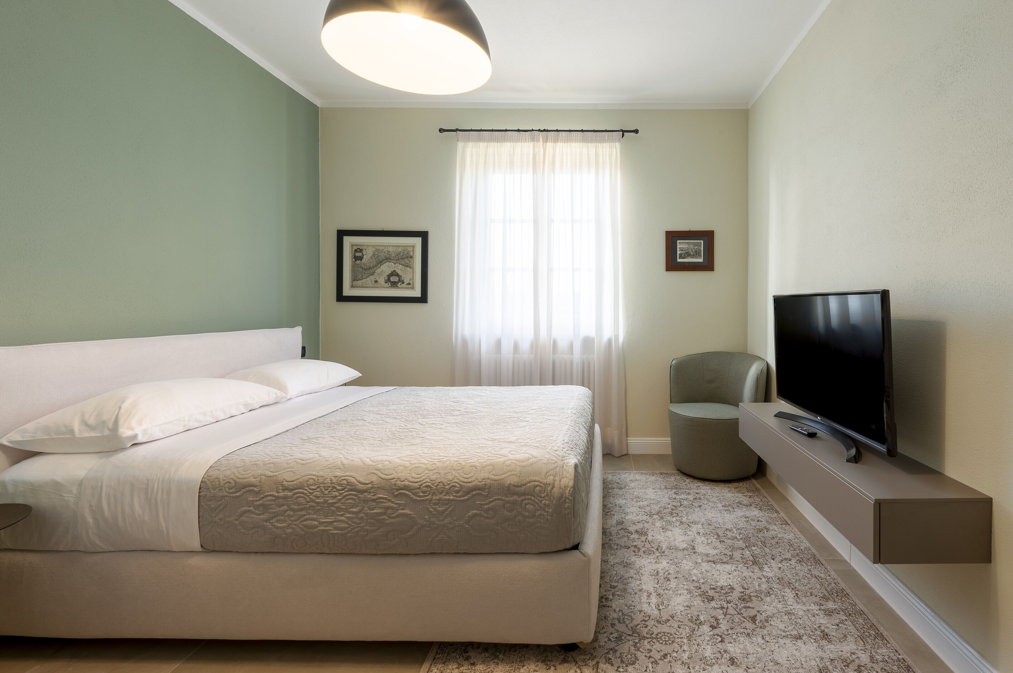 Een verzorgde slaapkamer met een bed, een televisie en een klein zithoekje.