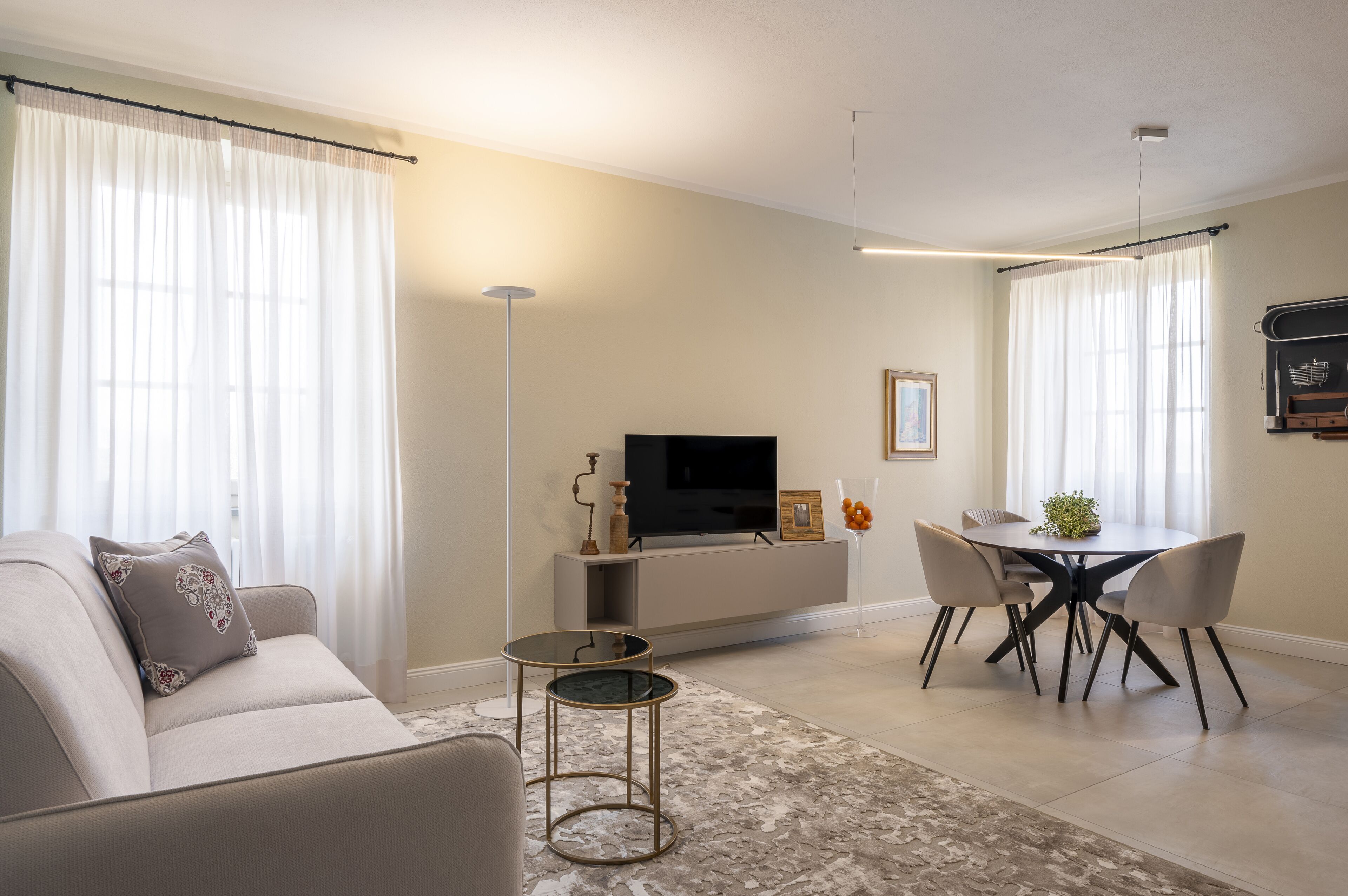 A modern living room with a sofa, a TV, a dining table with chairs, and a small side table.