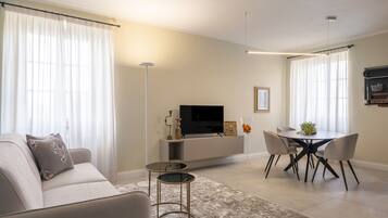 A modern living room with a sofa, a TV, a dining table with chairs, and a small side table.