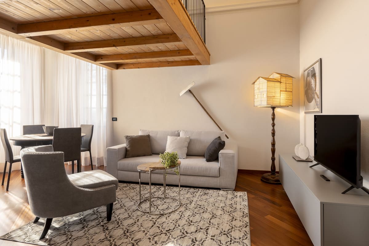 Ein Wohnzimmer mit Sofa, Sessel, Couchtisch, Fernseher, Lampe und einem Essbereich mit Stühlen und Tisch.