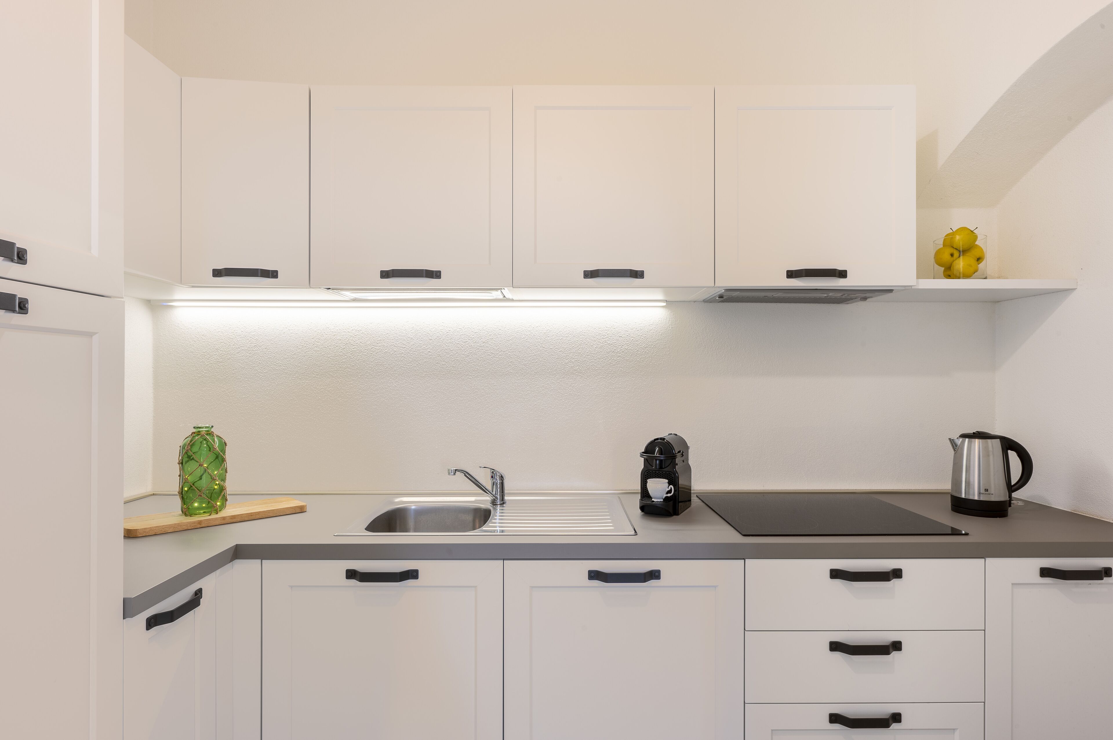A modern kitchen with white cabinets, a stainless steel sink, a coffee maker, and a kettle.