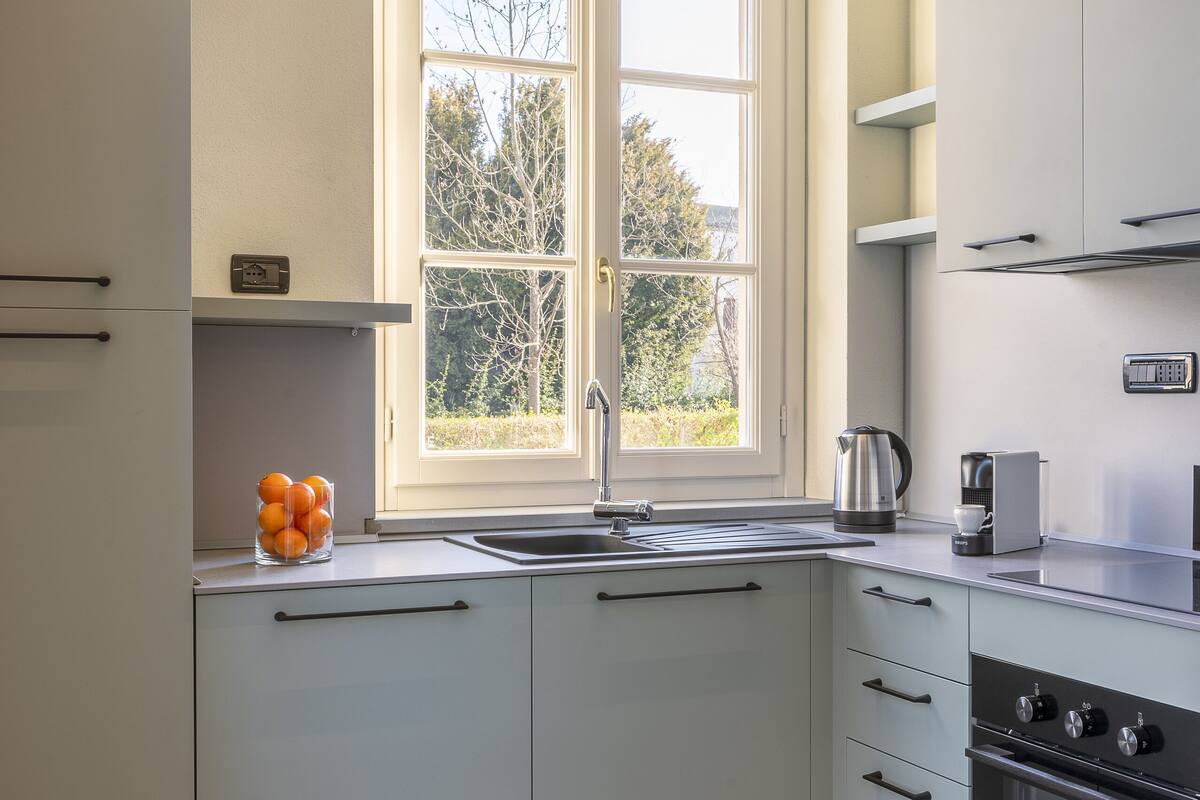 Eine moderne Küche mit weißen Schränken, einer doppelten Spüle und einem Fenster mit Blick auf Bäume.