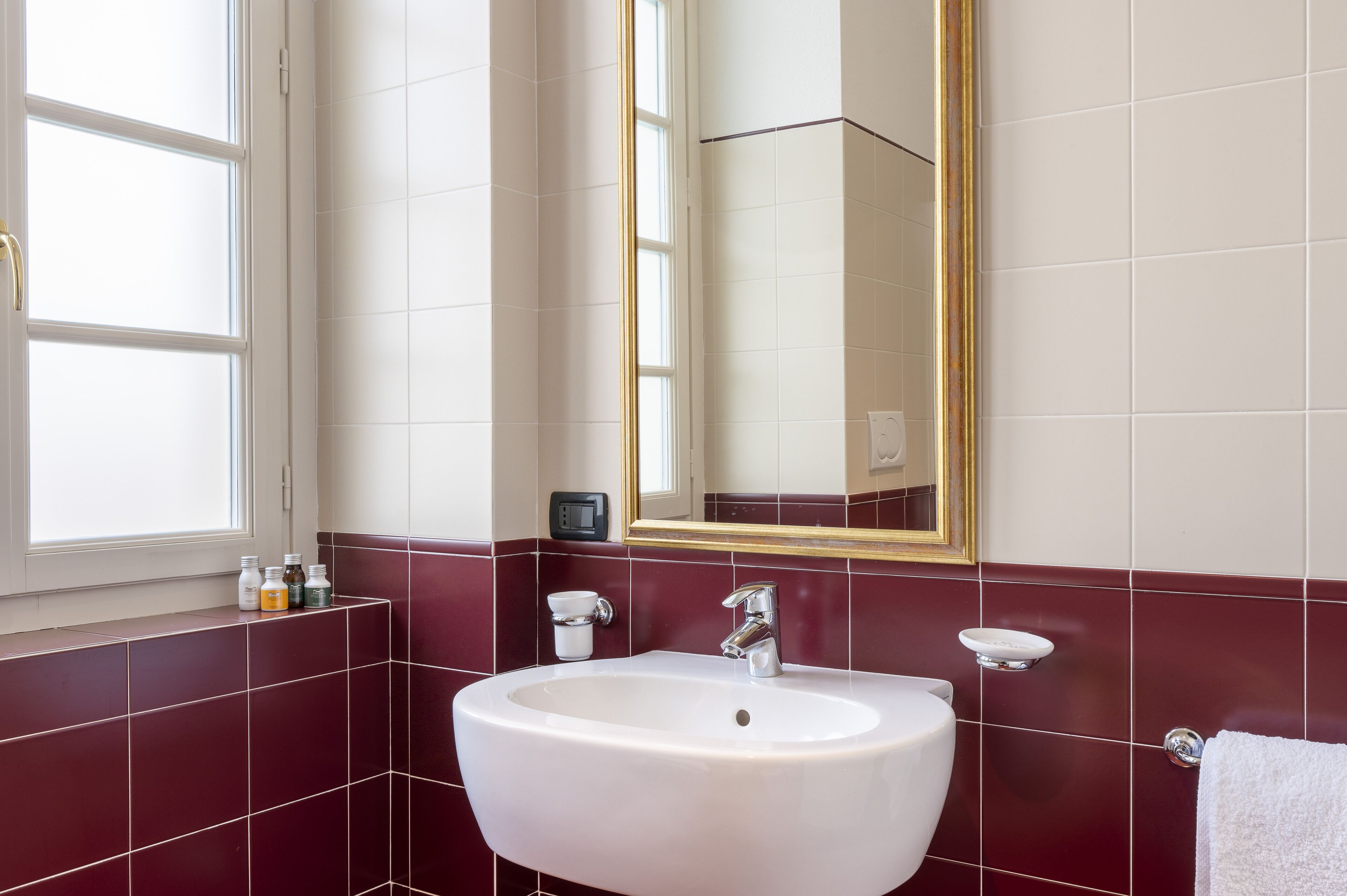 A bathroom with a white sink, a mirror with a gold frame, and red-tiled walls.