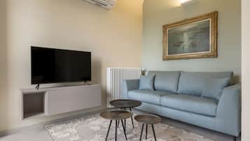 A modern living room with a flat-screen TV, a grey sofa, two round side tables, and a patterned rug.