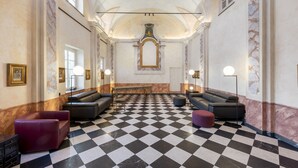 Un hall con piso a cuadros, sofás de cuero y una pared de mármol con una obra de arte enmarcada.
