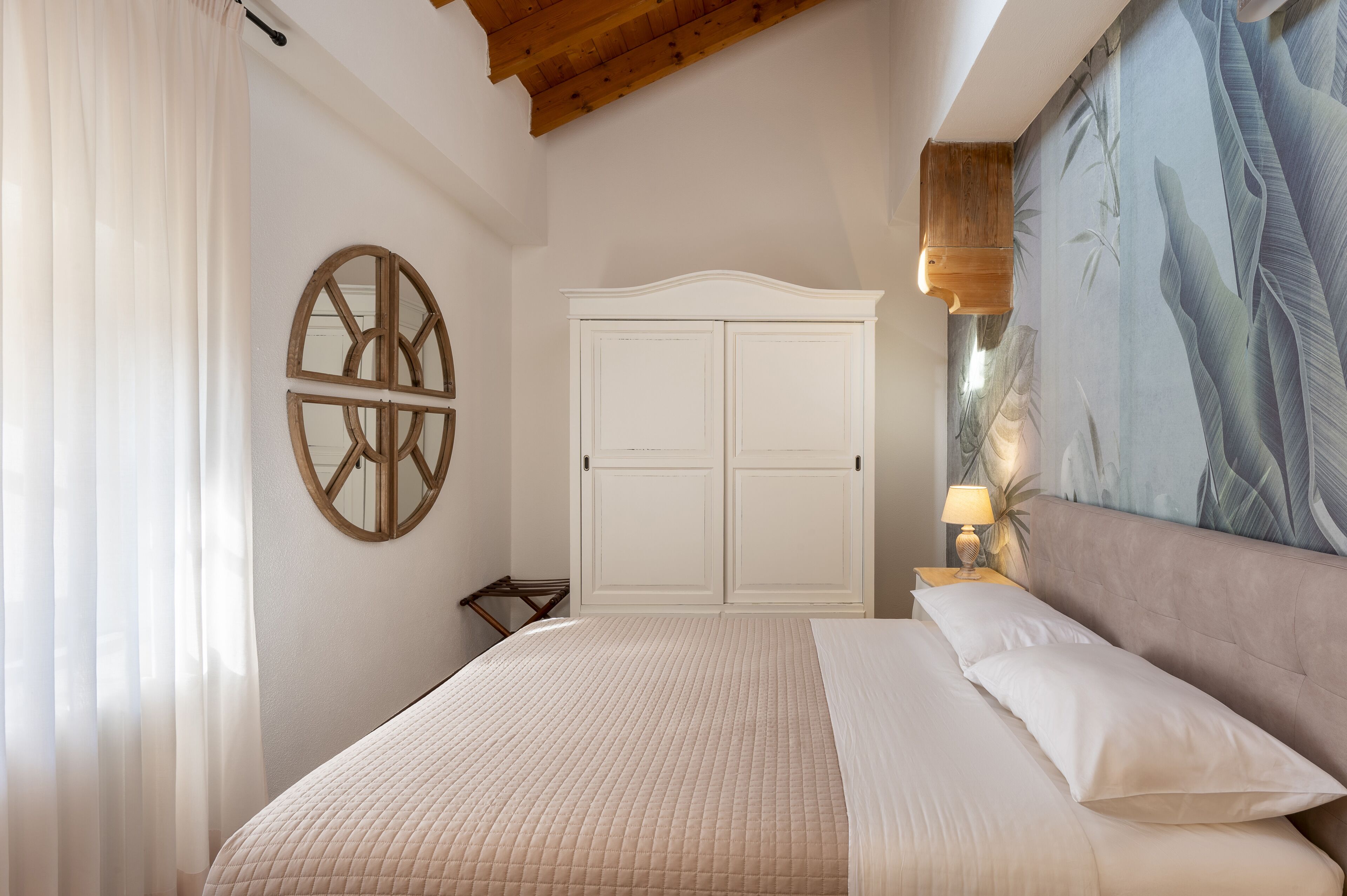 A bedroom with a bed, a wardrobe, a wall-mounted circular mirror, and a large painting.