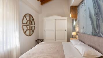 A bedroom with a bed, a wardrobe, a wall-mounted circular mirror, and a large painting.