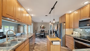 Una cucina moderna con mobili in legno, piani in granito, elettrodomestici in acciaio inossidabile e illuminazione a sospensione.