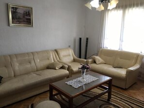 Una sala de estar con dos sofás de cuero color beige, una mesa de centro de madera con un jarrón decorativo, y un cuadro enmarcado en la pared.