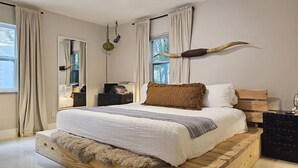 A modern bedroom with a wooden platform bed, a large mirror, and a unique wall decor piece.