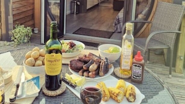 Un coin repas avec une table mise pour le dîner, comprenant une bouteille de vin, un saladier et des plats grillés.