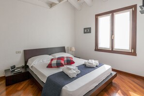 A neatly made bed with a checkered pillow, a bedside lamp, and a nightstand with a remote control. - Lugana Resort & Sporting Club - Sermana Village (Peschiera del Garda)