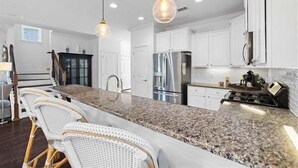 Una cocina con armarios blancos, encimera de granito y refrigerador de acero inoxidable.