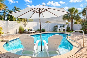 Une piscine avec deux chaises Adirondack, un parasol blanc et une clôture blanche en arrière-plan.