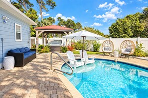 Un jardin avec une piscine, des chaises longues, un jacuzzi et un patio couvert.