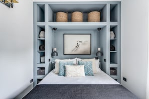 Un dormitorio moderno con cama, almohadas decorativas, una obra de arte enmarco y estantes empotrados con cestas.