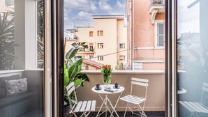A balcony with a table, chairs, a potted plant, and a view of neighboring buildings. - NEW COZY TERRACE VATICAN APT. (Roma)