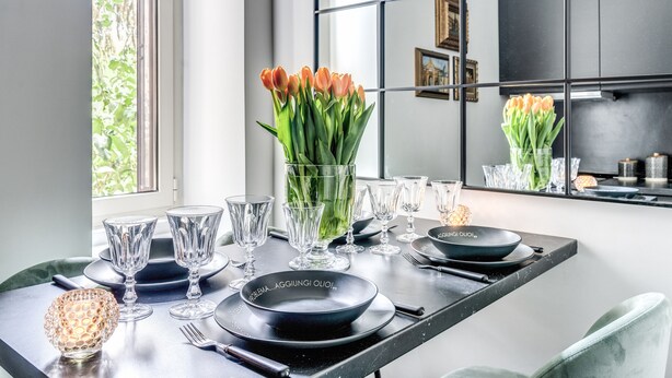 A modern dining area with a black table set for four, clear glassware, and a vase of orange tulips. - NEW COZY TERRACE VATICAN APT. (Roma)