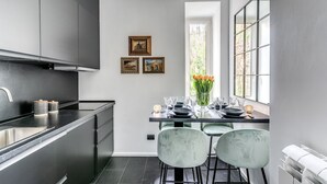 A modern kitchen with dark cabinetry, a stainless steel sink, and a dining area with a table set for four. There are three framed pictures on the wall, and a window with a view of greenery. - NEW COZY TERRACE VATICAN APT. (Roma)