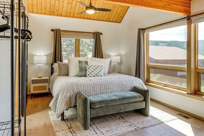Une chambre à coucher avec un lit, des lampes de chevet, un banc, une fenêtre donnant sur un beau paysage et un ventilateur de plafond.
