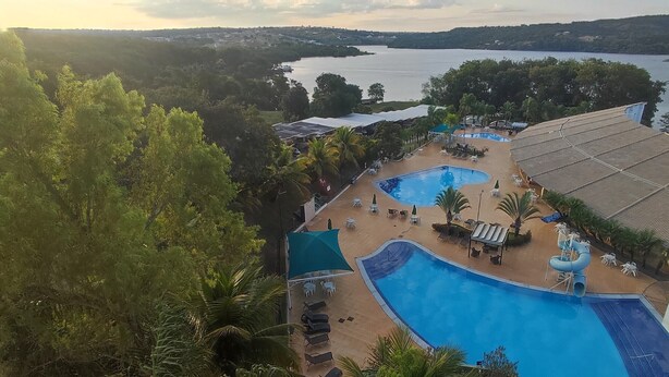 A resort with a large swimming pool, sun loungers, and a view of a lake. - HotFérias Flat Enseada pesca permitida (Caldas Novas)