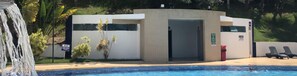 A pool area with a water feature, a small building with a door, and lounge chairs.