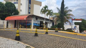 A hotel entrance with a red awning, chain barriers, and a sign for 'HotFérias Ingressos & Hospedagem'.