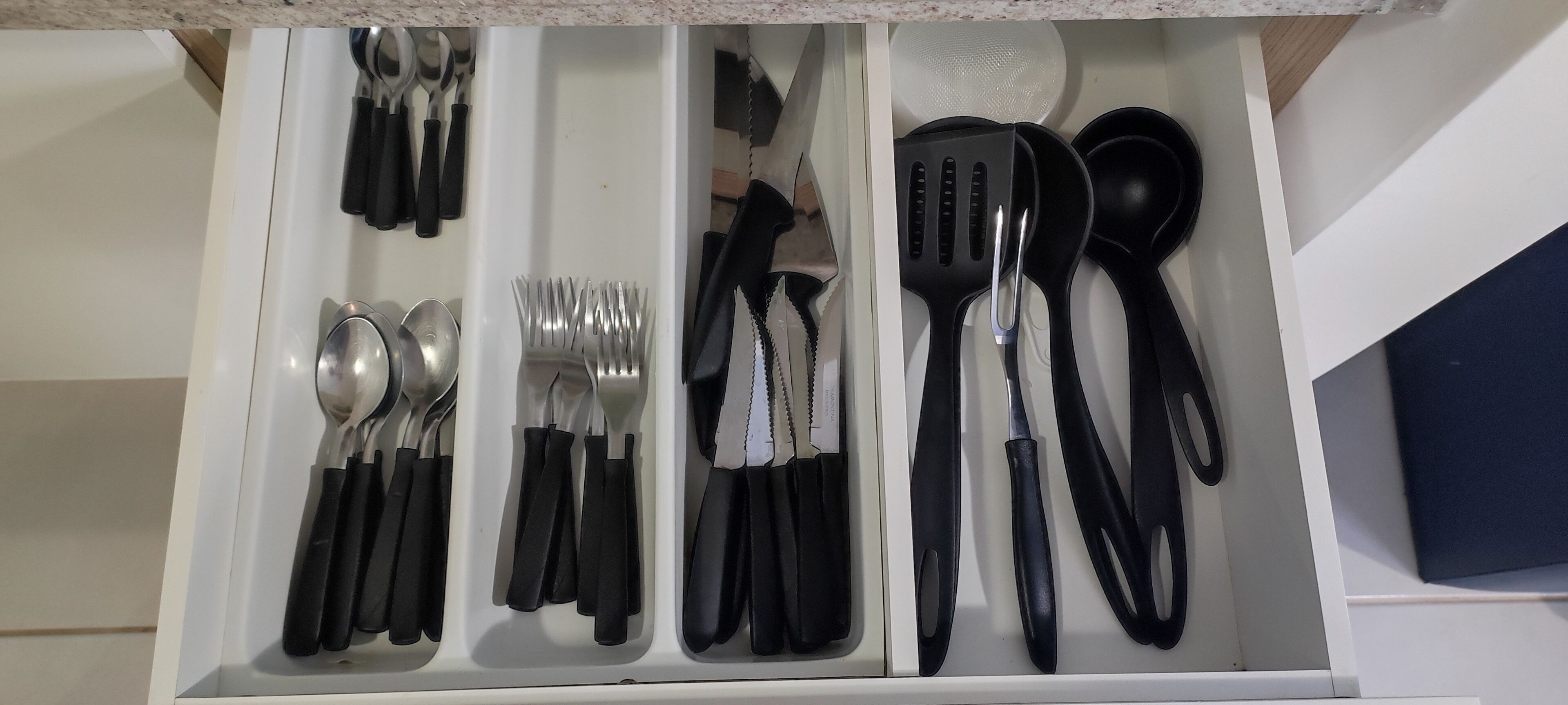 A kitchen drawer with utensils neatly organized, including spoons, forks, knives, spatulas, and a grater.