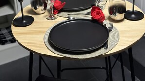 Ruokapöytä on katettu mustilla lautasilla, hopeaesineillä ja laseilla. Pöydällä on myös kynttilöitä ja punainen ruusu. Pöytä on puuta, ja se sijaitsee modernissa keittiössä.