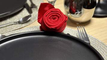Et bord dækket med en sort tallerken, en rød rose, et vinglas og et vandglas.
