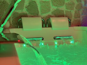 A bathtub with two faucets and a stone wall in the background.